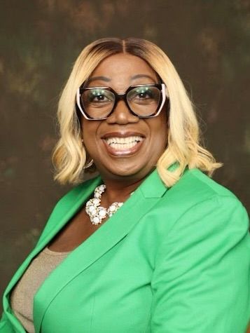 A woman wearing glasses and a blue shirt is smiling.