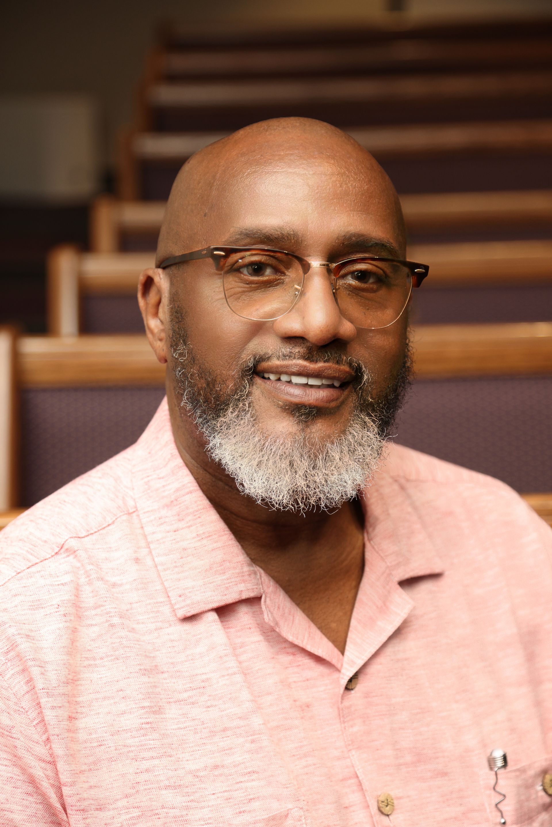 A man with a beard and glasses is wearing a pink shirt.