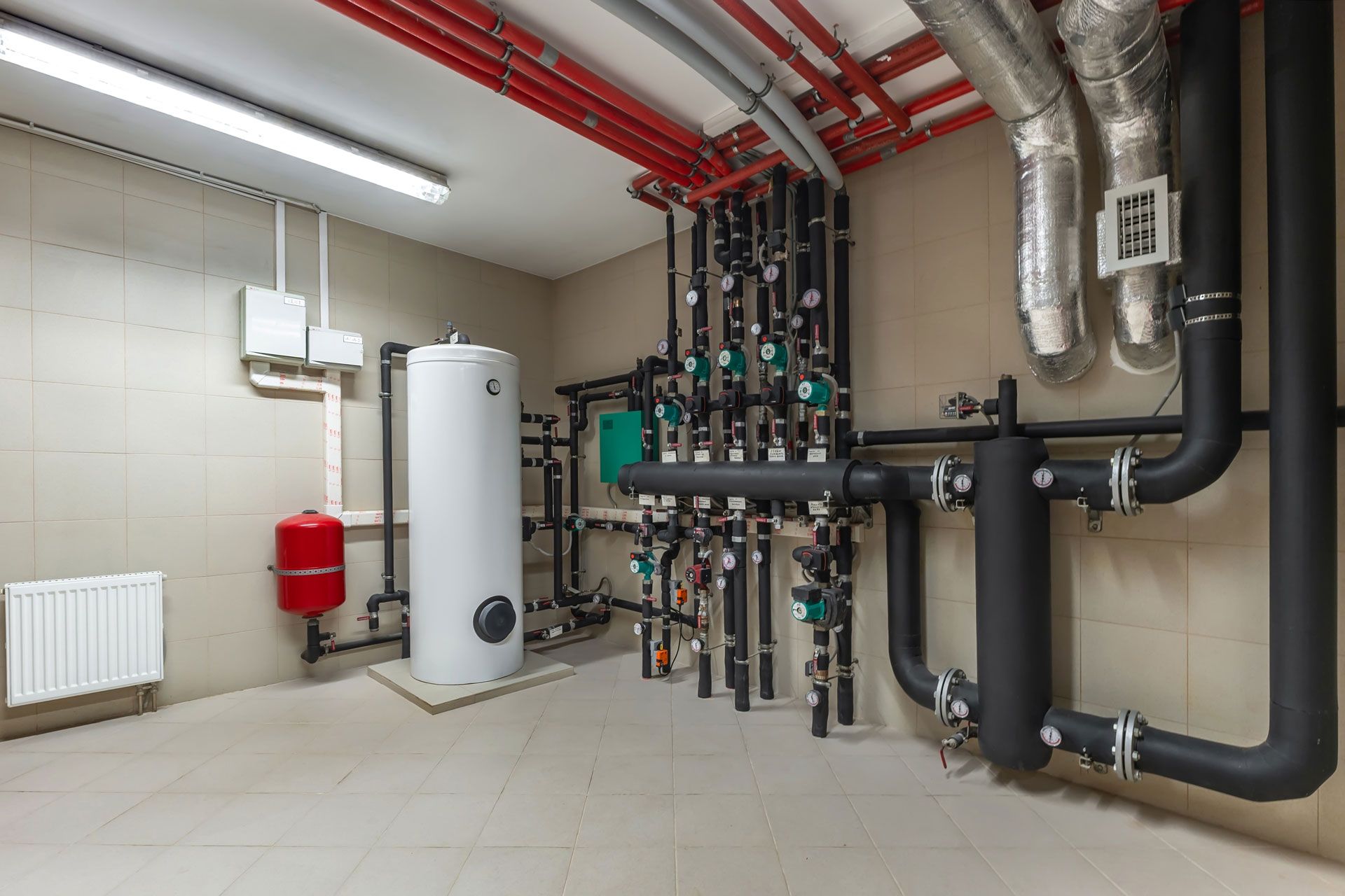 Mechanical room with pipes, valves, boiler, and water tanks along tiled walls and ceiling.