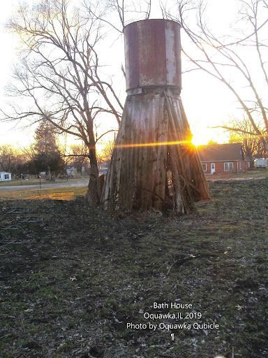 Old weathered bath house tower at sunset, with leafless trees and a glowing horizon.