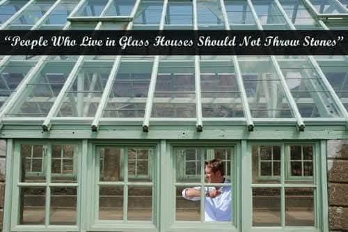 Person in white shirt standing in greenhouse beneath a banner reading, “People Who Live in Glass Houses Should Not Throw Stones”
