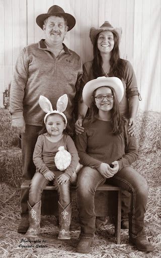 Family portrait in cowboy hats, with two adults standing behind two seated children in a rustic indoor setting