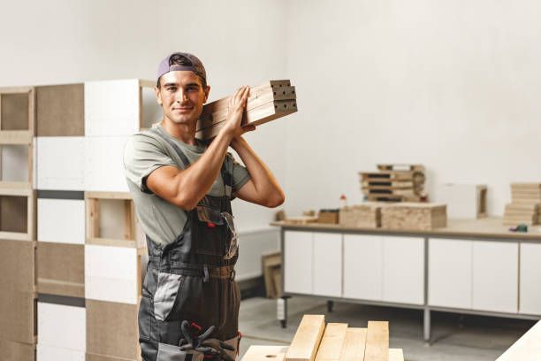 Smiling carpenter carrying wood planks in a workshop.
