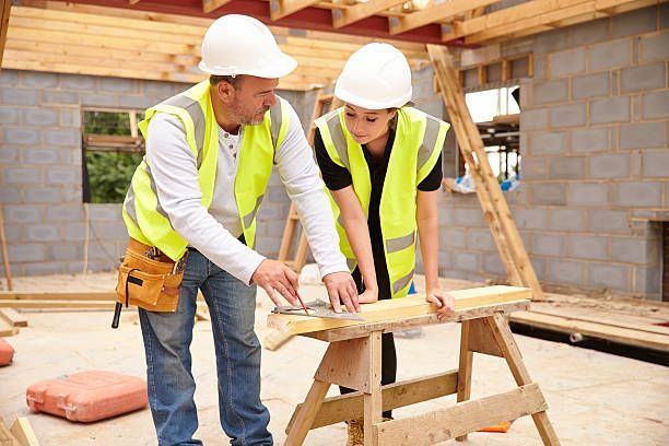 Carpenters in hard hats measuring wood on a site.