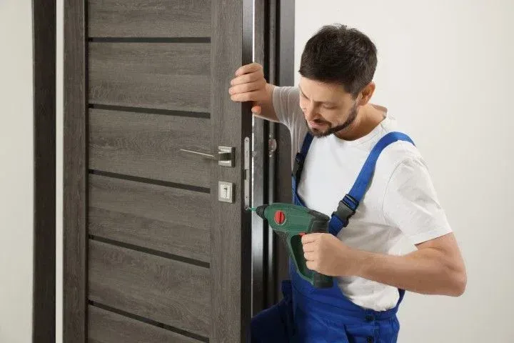 Handyman installing a dark wooden door with a drill