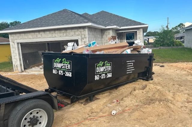 Dumpster in a driveway beside a house under construction, filled with renovation debris.