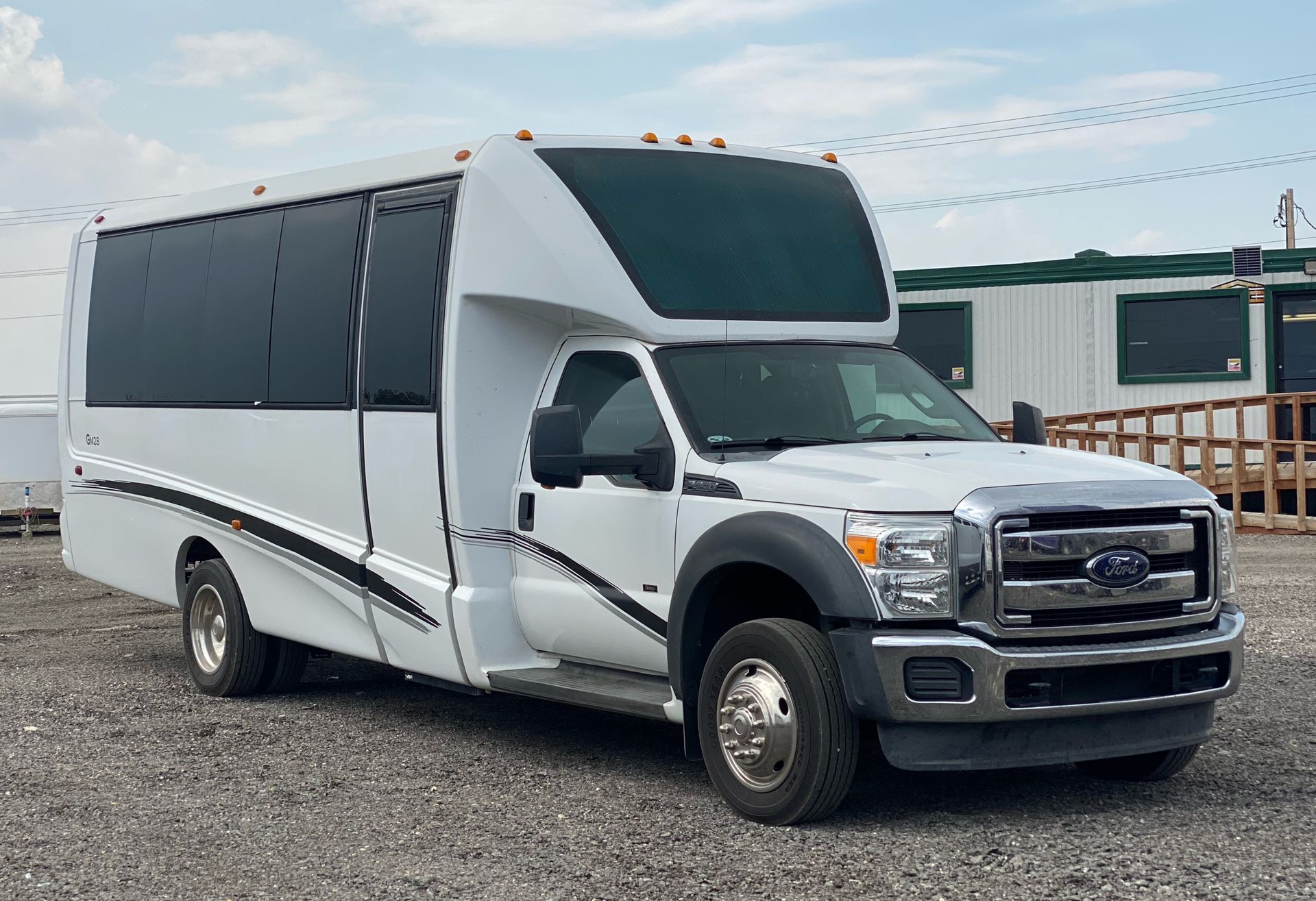a white 20 passenger executive shuttle bus is parked in a gravel lot .