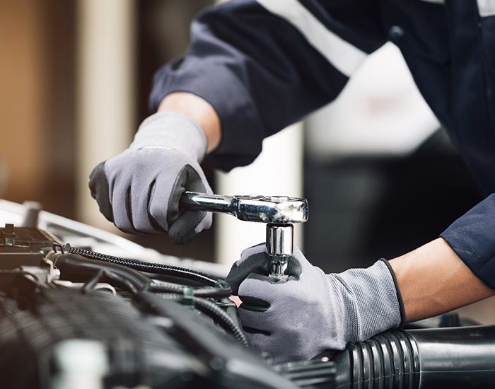 Gloved hand pouring motor oil into a car engine bay during maintenance