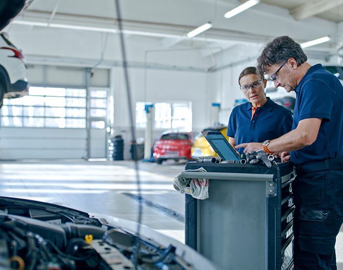 Mechanic inspecting a car engine while writing notes on a clipboard in a garage