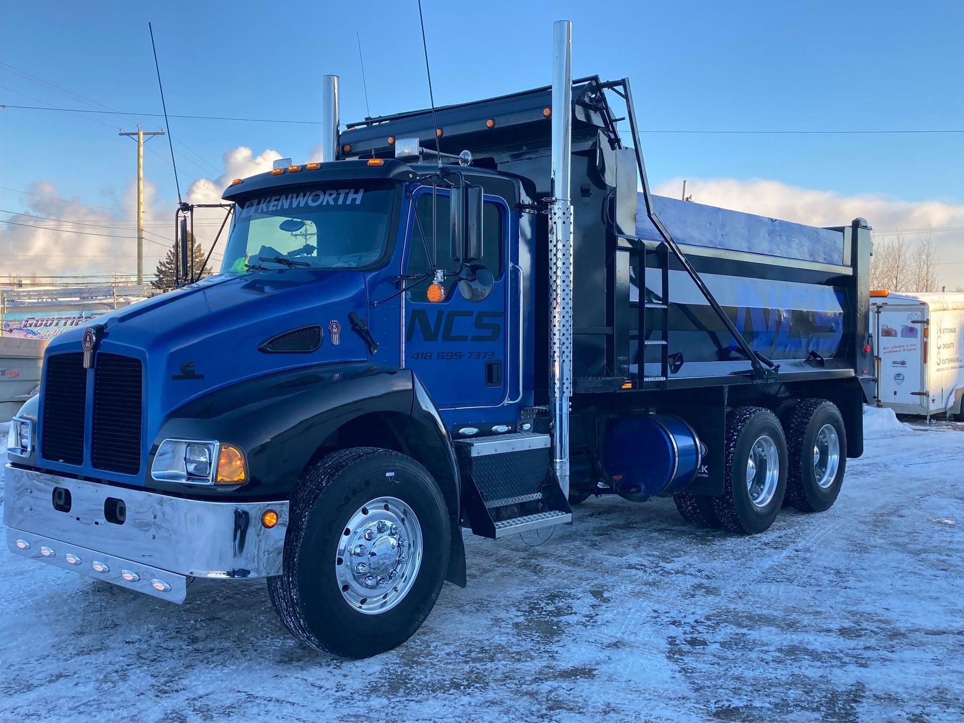 Un camion-benne bleu est garé dans la neige.