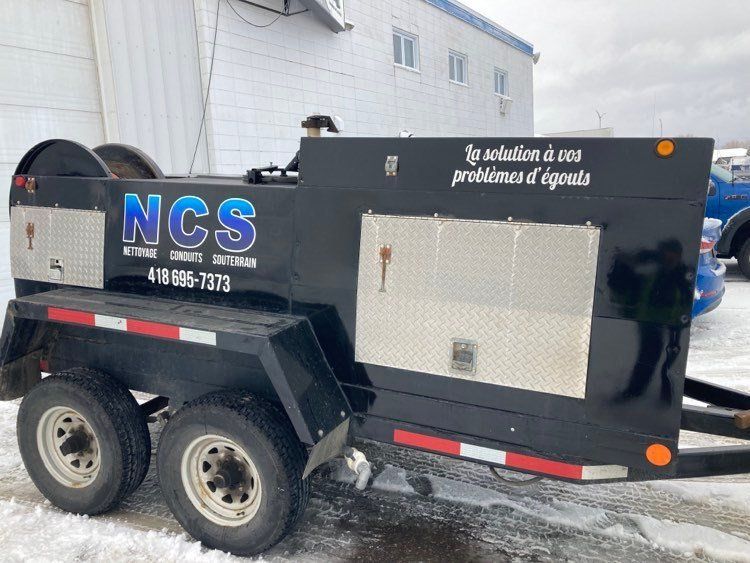 Une remorque noire avec NCS écrit dessus est garée dans la neige.