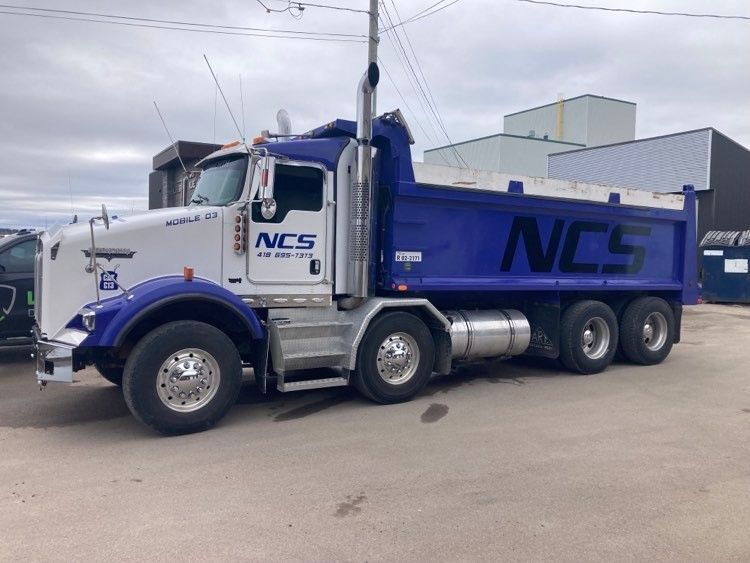 Un camion-benne bleu et blanc est garé sur un parking.