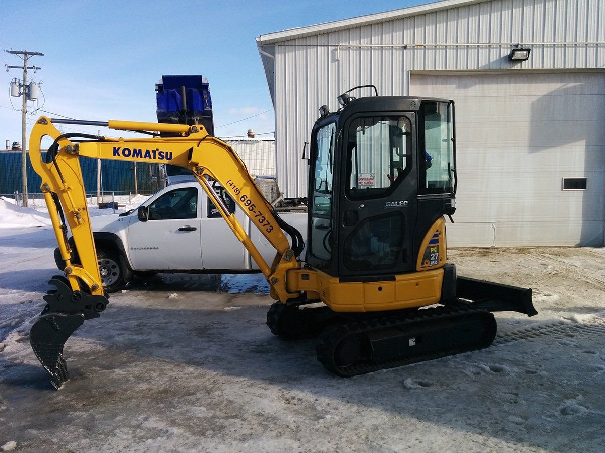 Une excavatrice Komatsu jaune est garée à côté d'un camion blanc