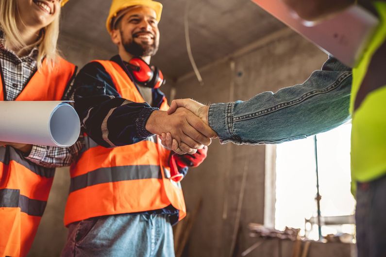 A group of construction workers are shaking hands on a construction site.