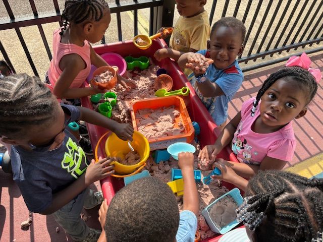 Children playing with sand in a red sandbox, using toys.