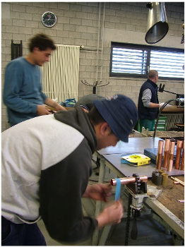 Persone al lavoro ai banchi di un'officina, intente ad assemblare o riparare attrezzature.