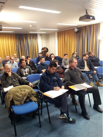 Il pubblico è seduto in una sala riunioni e ascolta con i taccuini in mano.