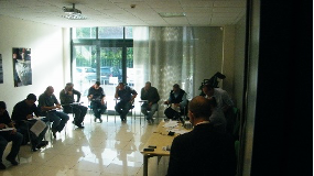 Persone sedute attorno a un tavolo in una luminosa sala conferenze, riunite vicino a grandi finestre.