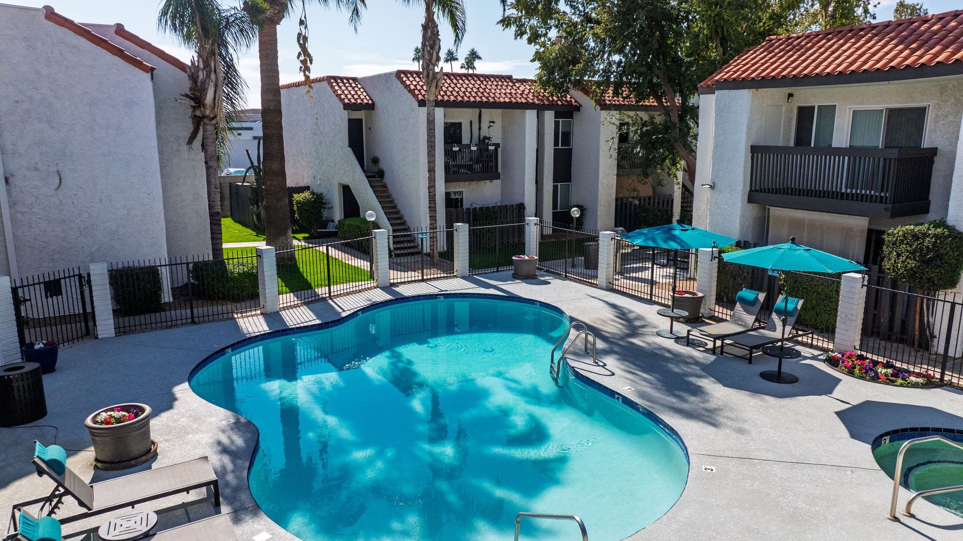 Swimming pool surrounded by two-story apartments with red tile roofs. Lounge chairs and umbrellas.