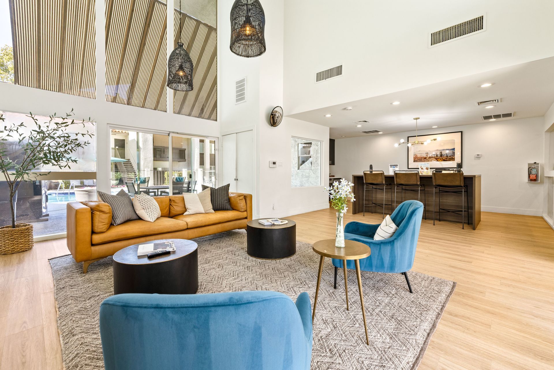 Lounge area with high ceilings, large windows, couches, blue chairs, bar, and outdoor pool view.