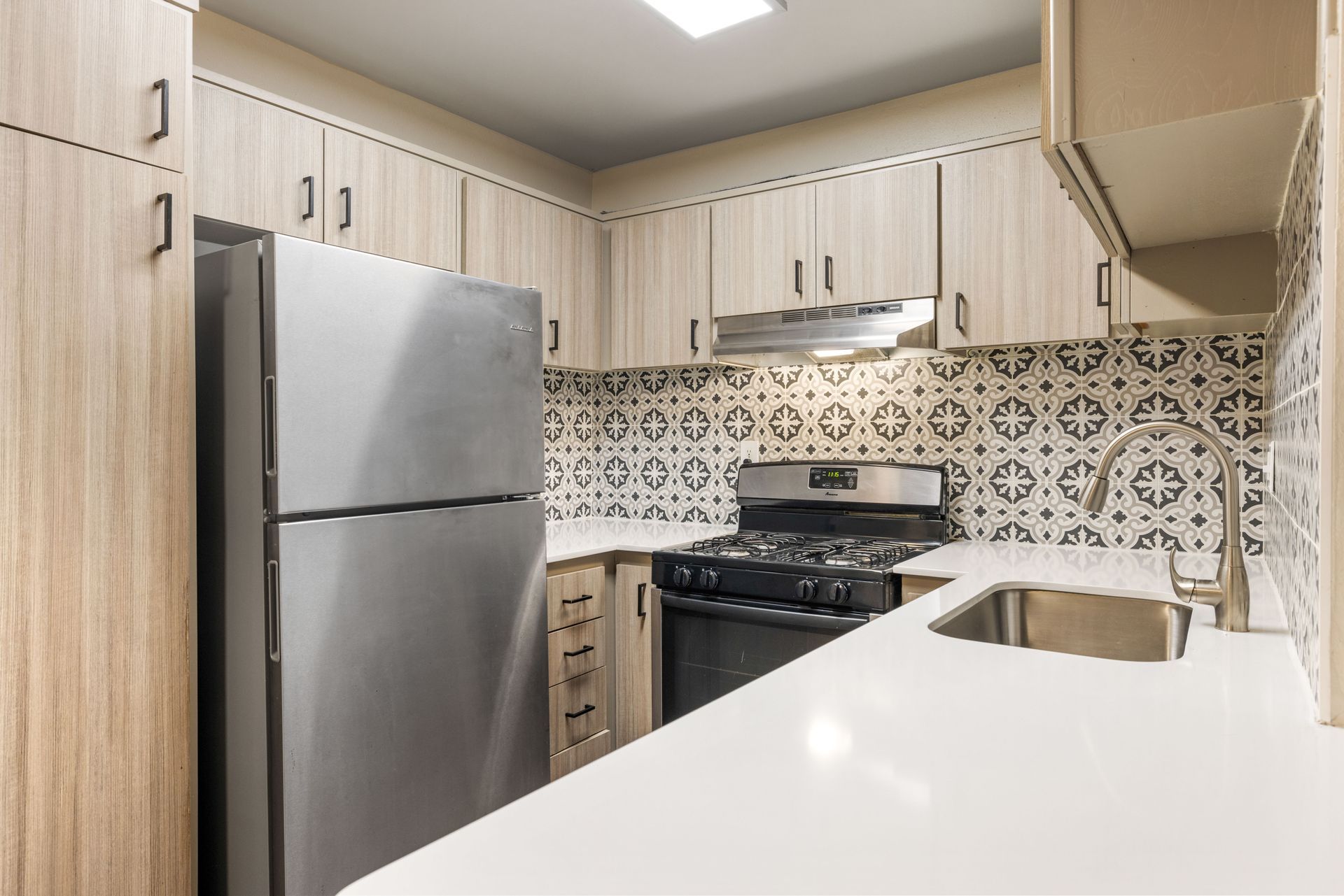 Kitchen with light wood cabinets, stainless steel appliances, and patterned backsplash.