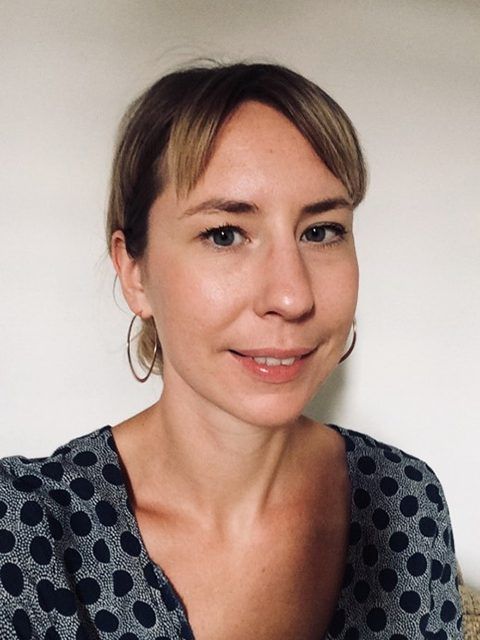 Portrait of a woman with short hair wearing a patterned blouse, looking at the camera against a plain background
