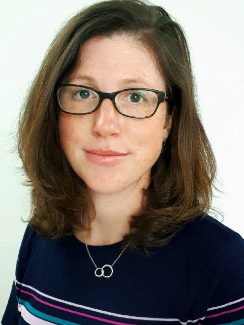 Portrait of a woman with glasses wearing a navy top and necklace against a light background
