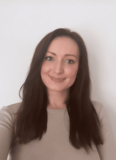 Person with long dark hair smiling in a beige top against a plain white background