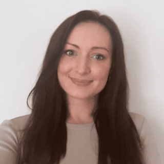 Woman with long dark hair smiling in a beige top against a plain white background