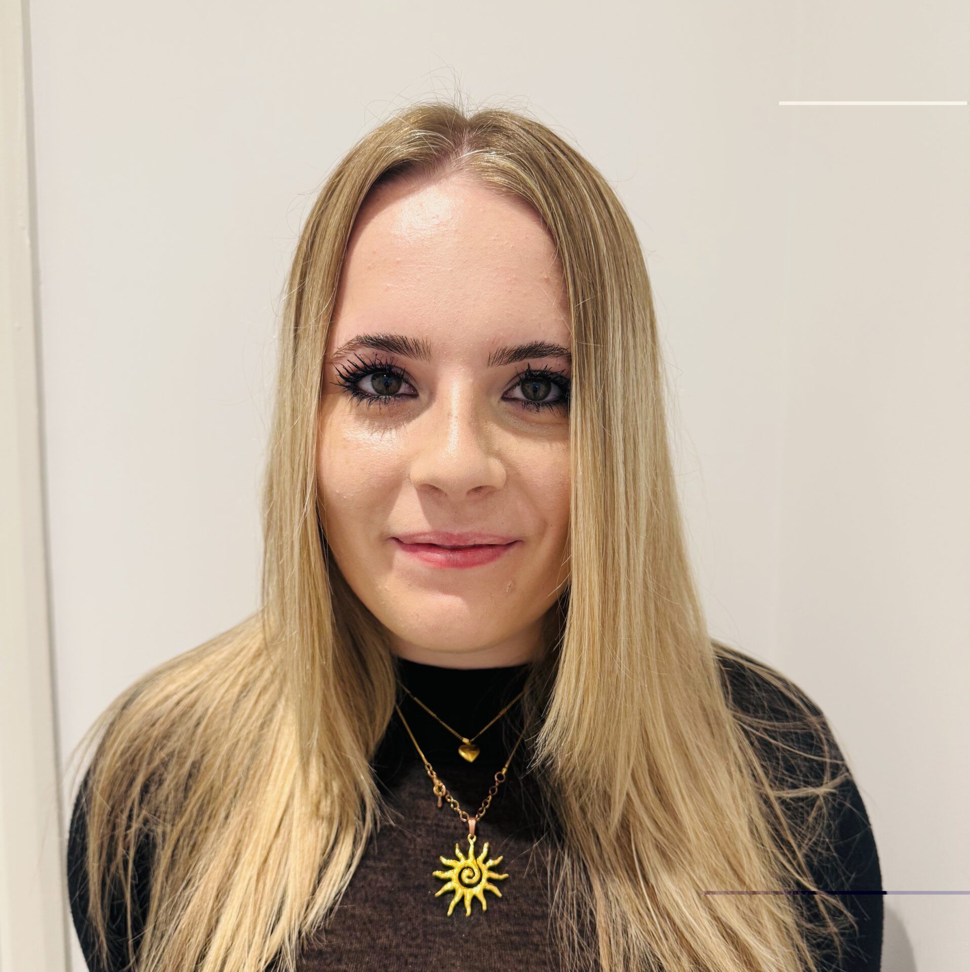 Portrait of a smiling woman with blonde hair wearing a black top and gold sun necklace