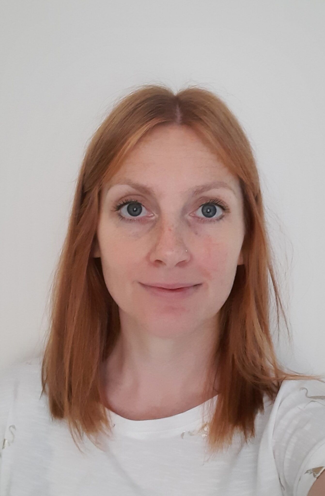 Portrait of a woman with red hair wearing a white shirt against a plain background