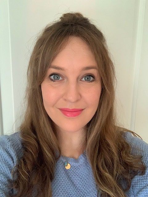 Portrait of a smiling woman with long brown hair wearing a light blue sweater and gold necklace