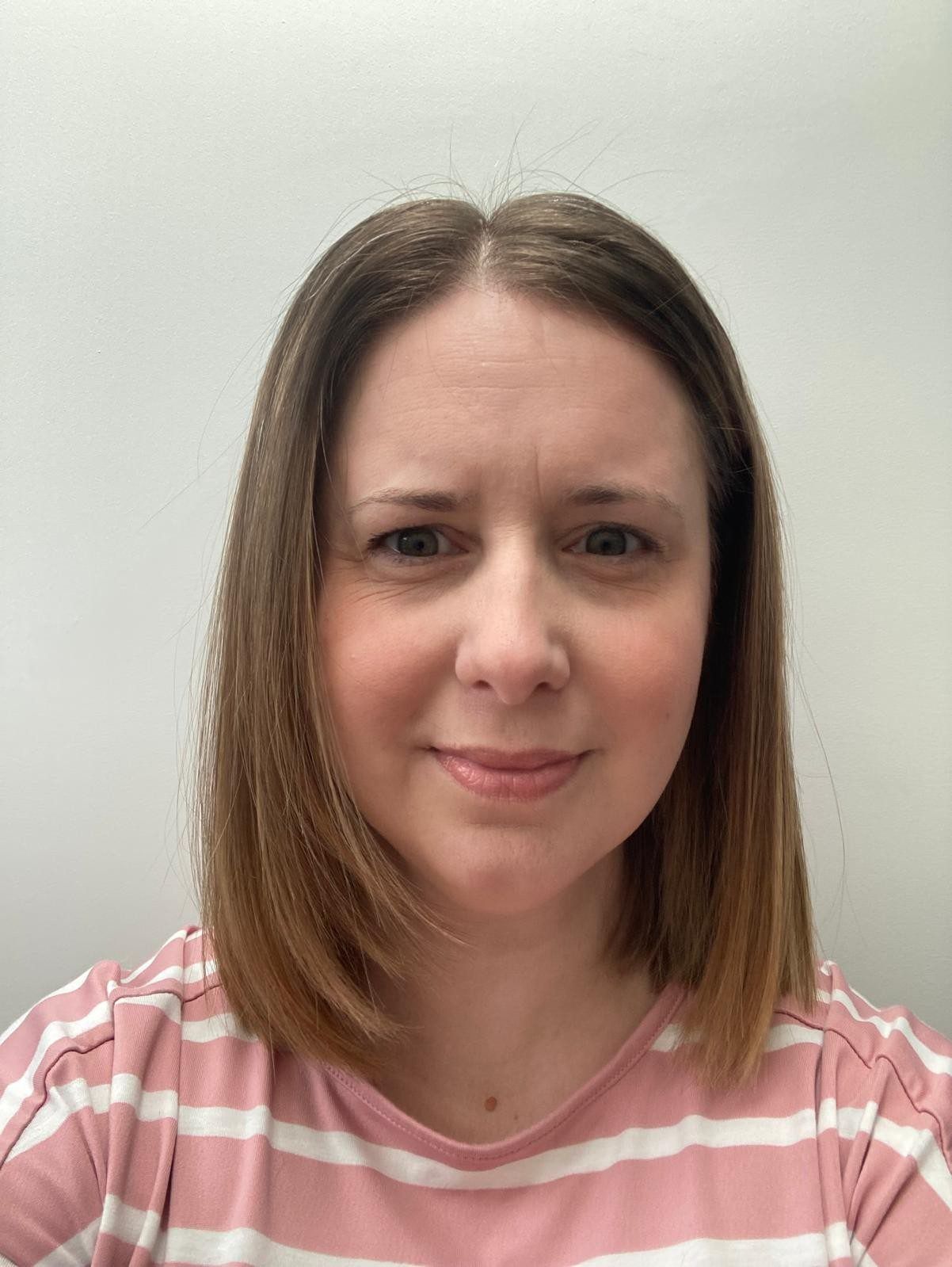 Woman in a pink striped shirt looking at the camera against a plain light wall.