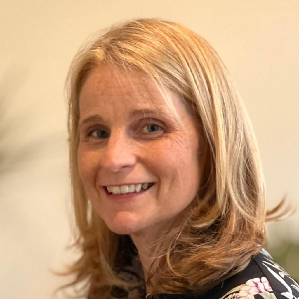 Smiling blonde woman in a black floral top against a warm beige background