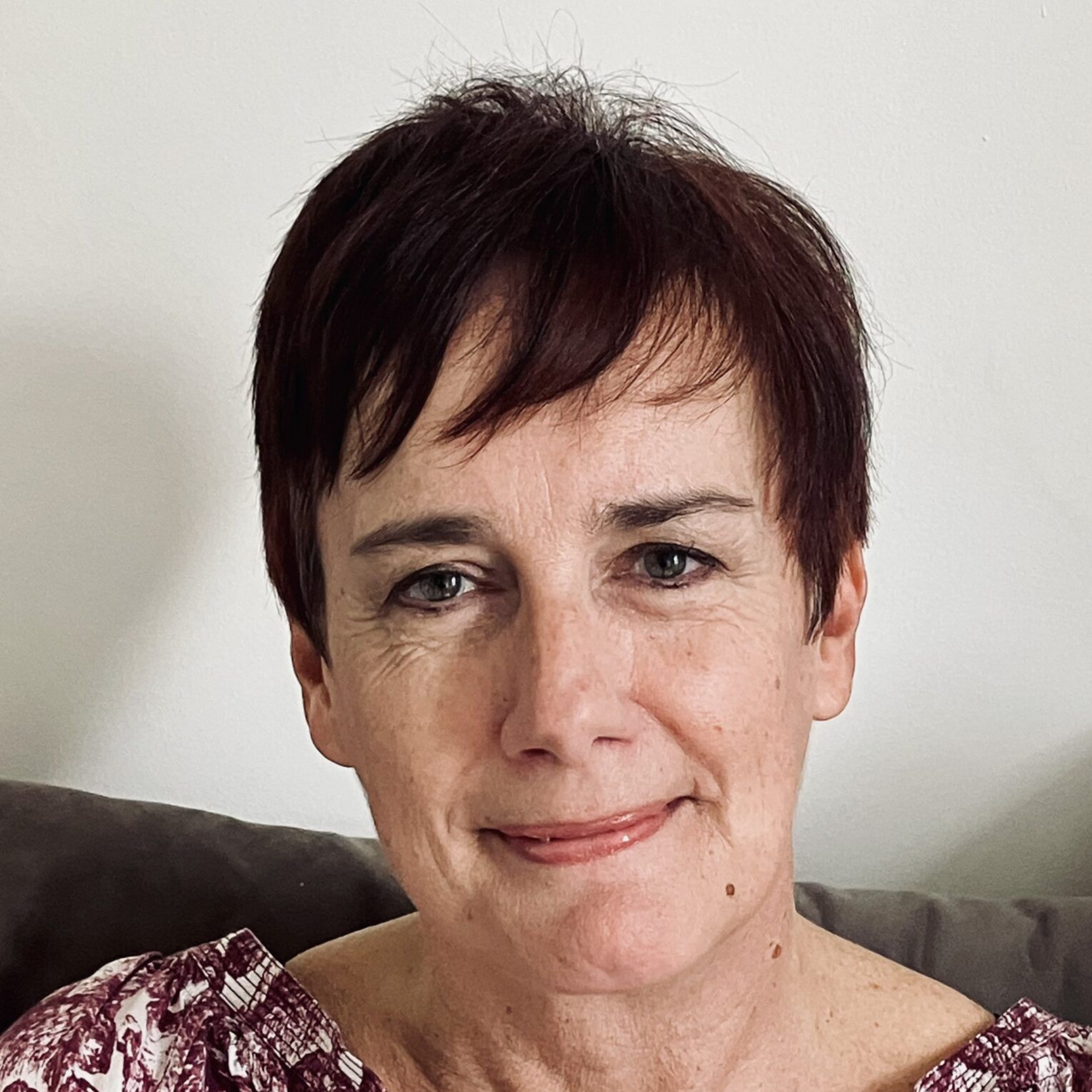 Portrait of a smiling person with short dark hair against a plain light wall