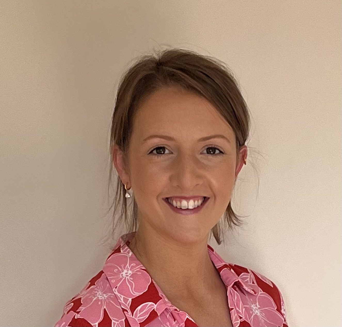Portrait of a smiling woman in a pink patterned blouse against a beige wall