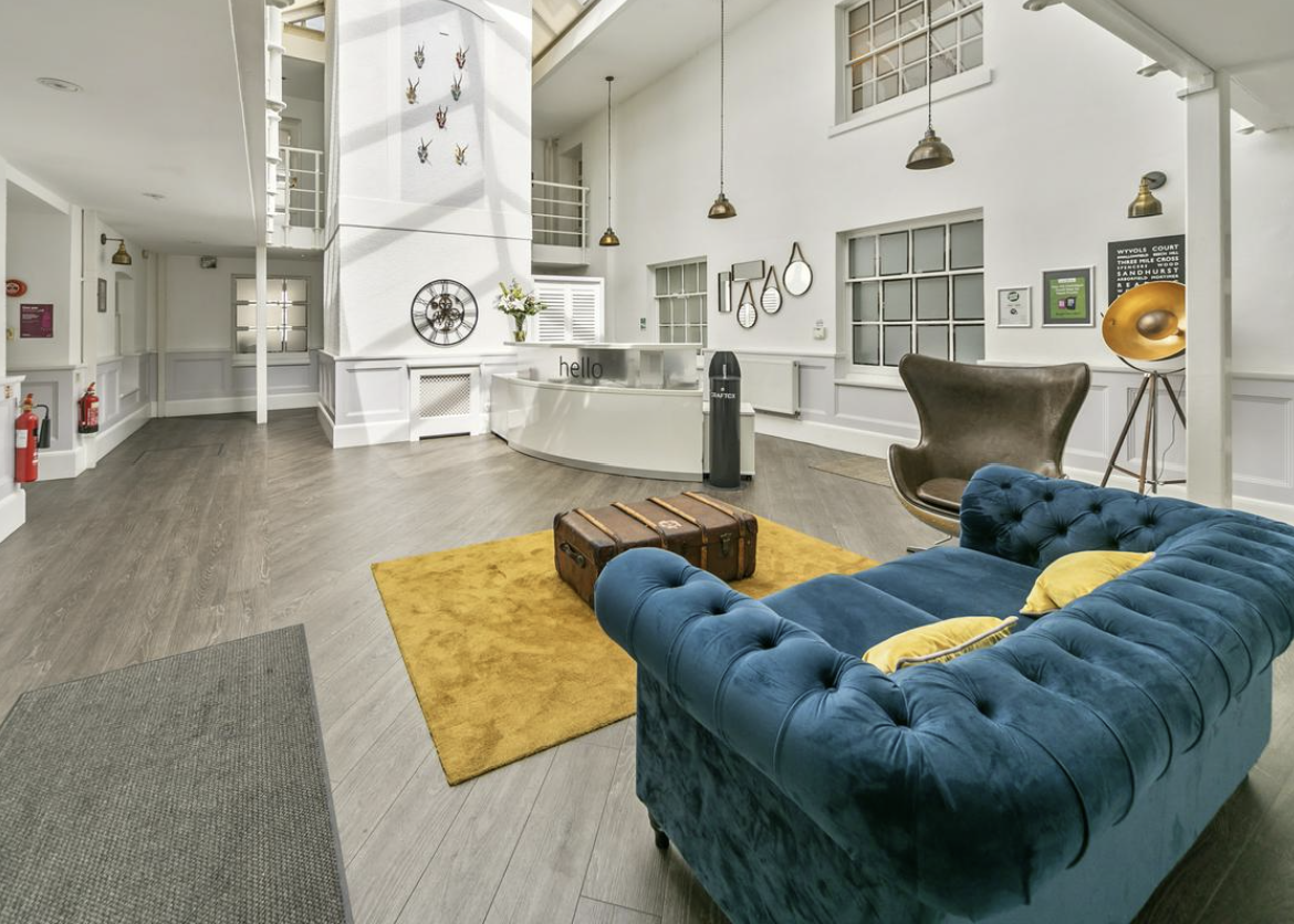 Bright modern living room with white walls, gray floors, blue tufted sofa, yellow rug, and large windows.