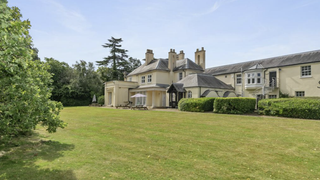 Large stone country house with a manicured lawn and trees on a sunny day