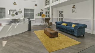 Bright modern living room with blue sofa, mustard rug, coffee table, and open kitchen area.