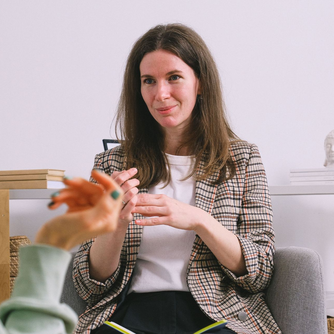 Woman seated on a sofa, smiling and holding a patterned cup in a bright living room.