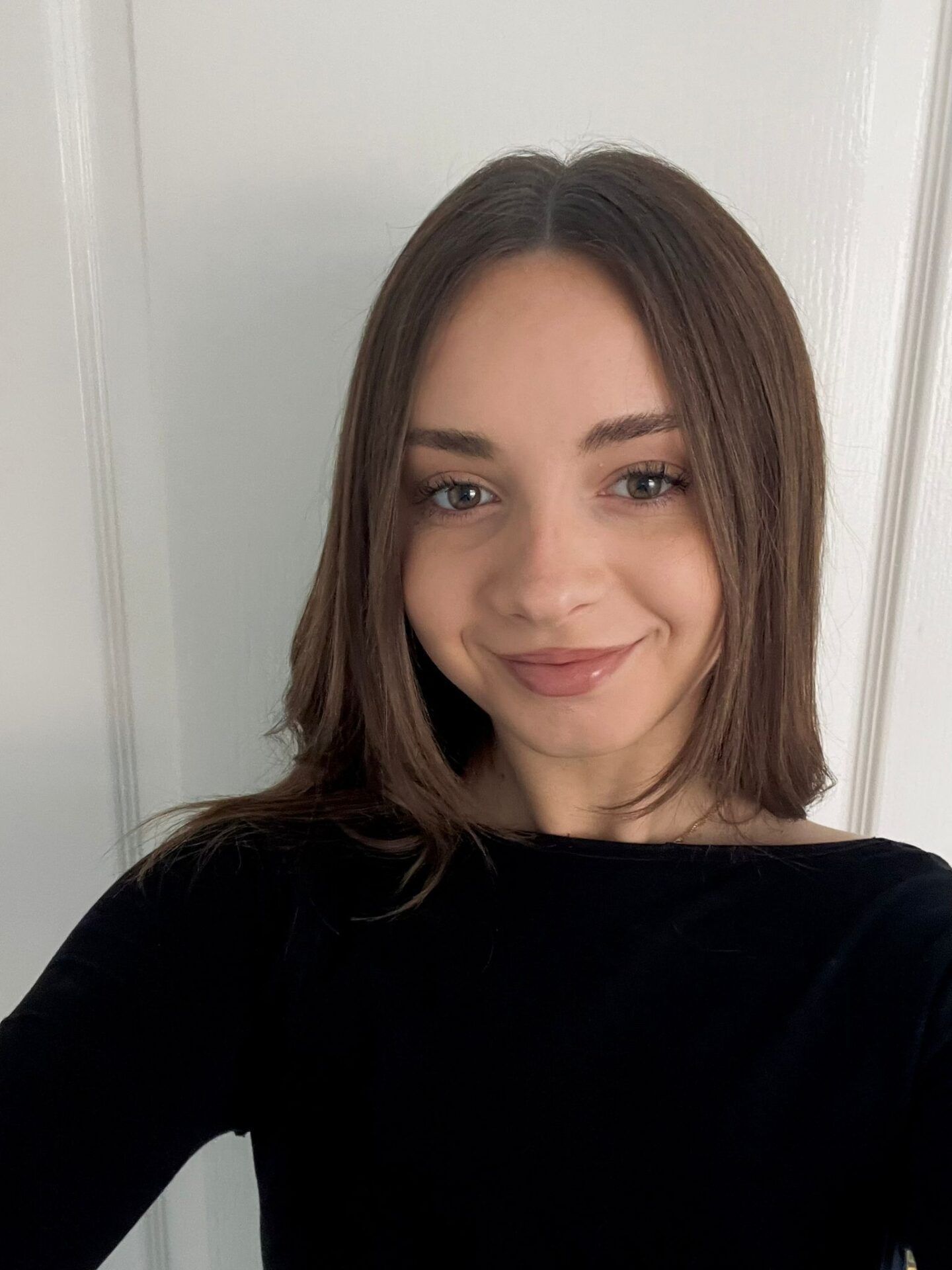 Portrait of a smiling person in a black top against a light wall.