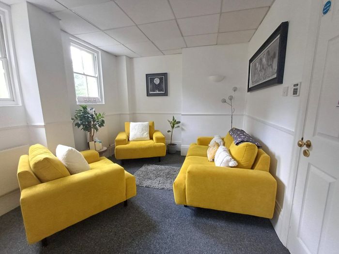 Bright lounge with yellow sofas, armchairs, white walls, and framed art in a sunlit room