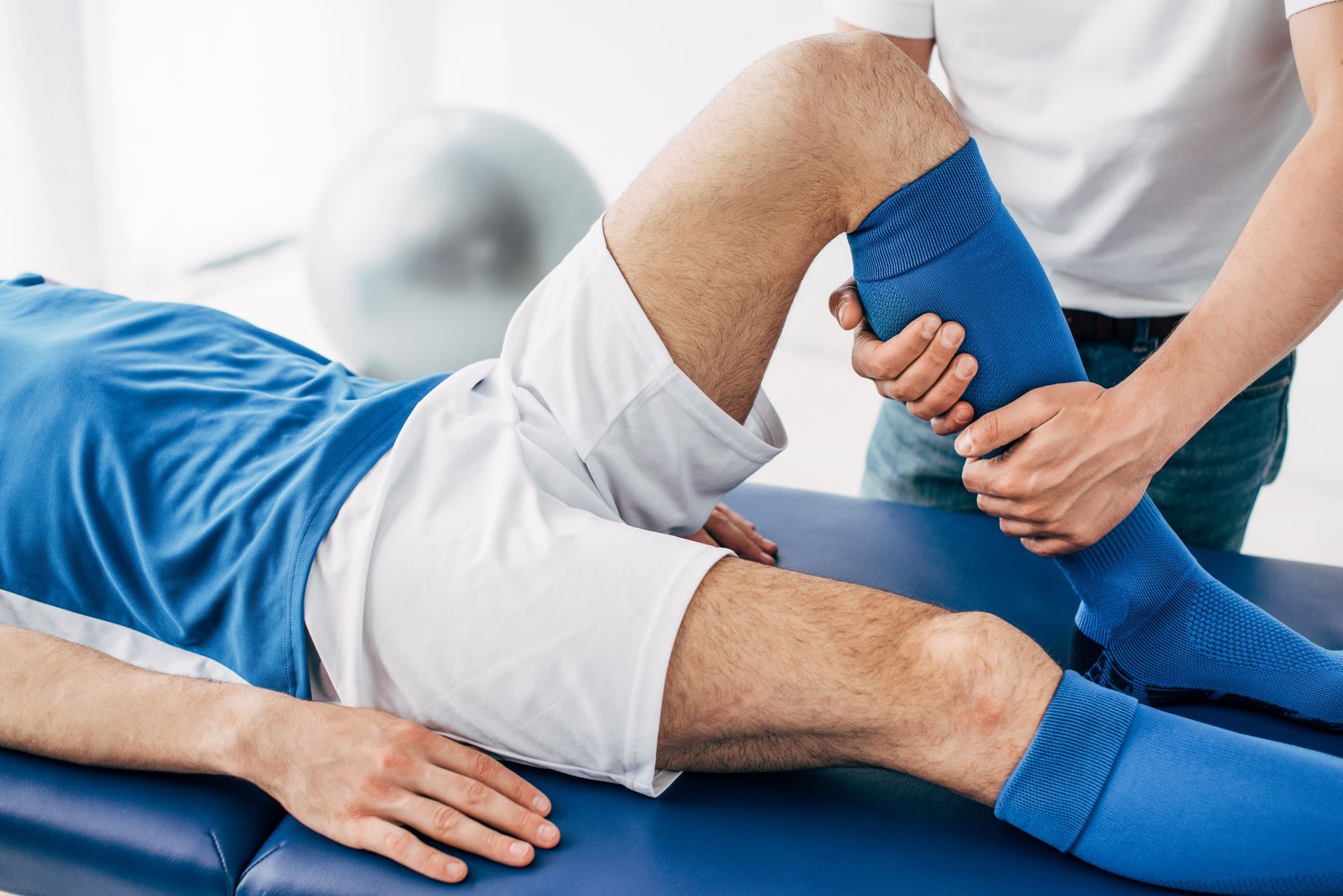 a medical professional holds and moves the patient's leg while they lie on a medical bed.