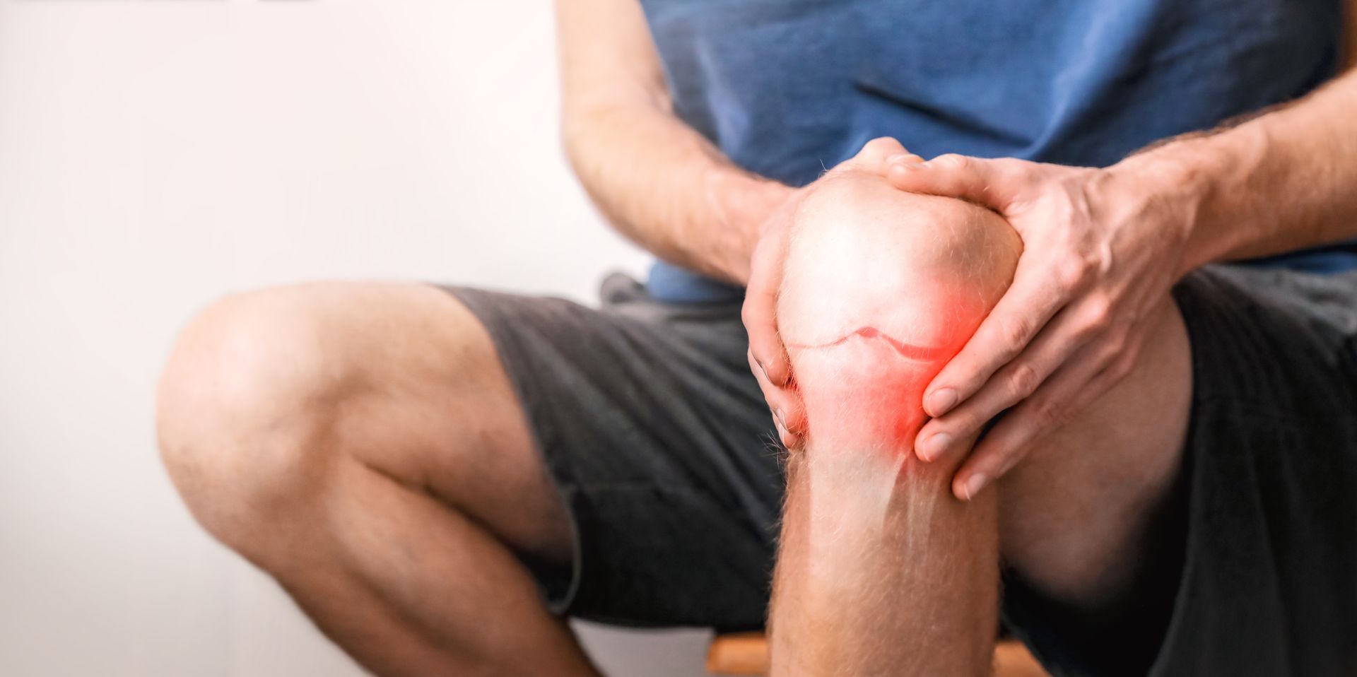 A person holding their knee, indicating pain. The knee is highlighted with a red glow.