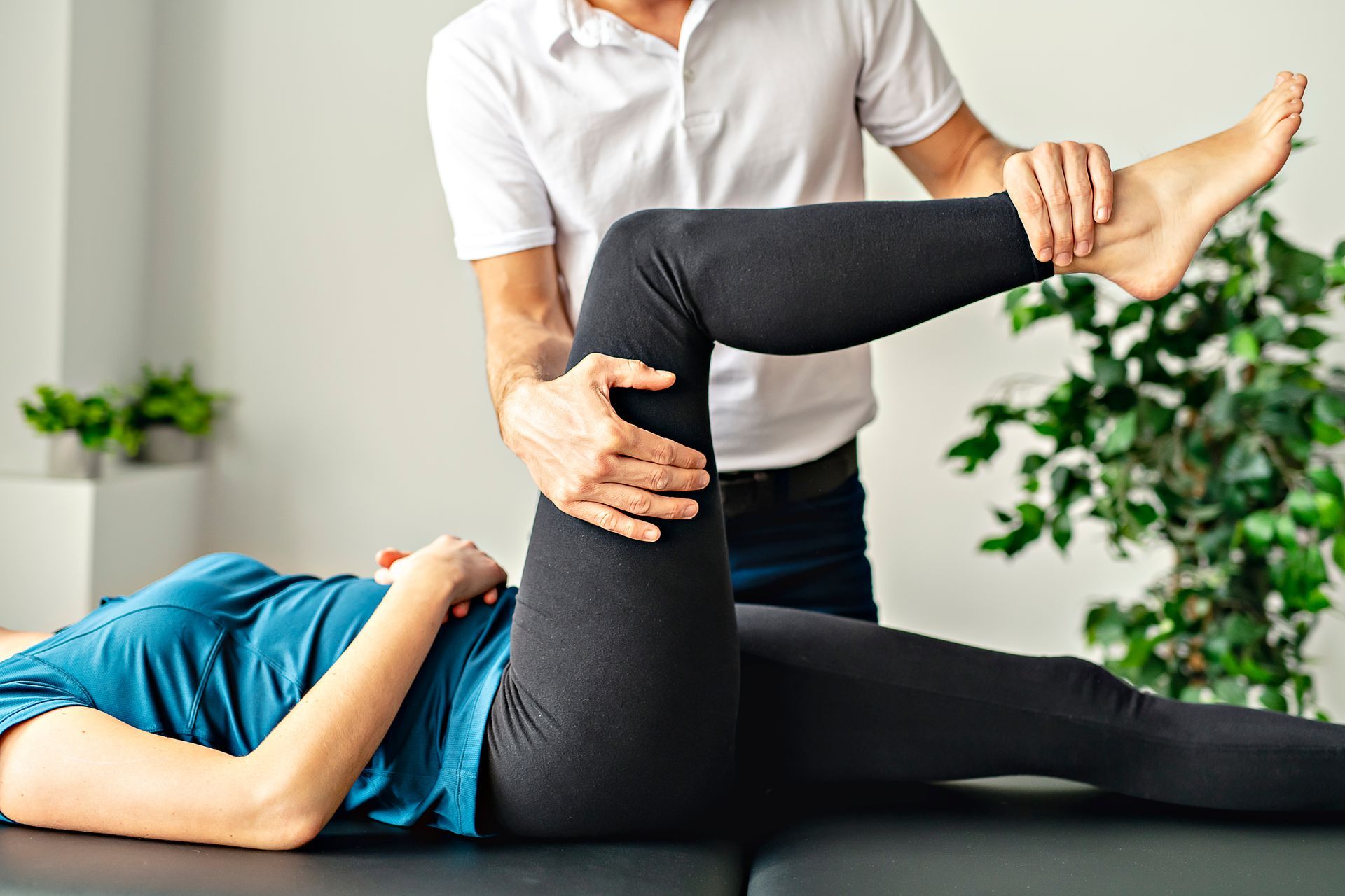 A physical therapist extends a patient's leg, assessing movement while the patient lies on a treatment table in a clinic.