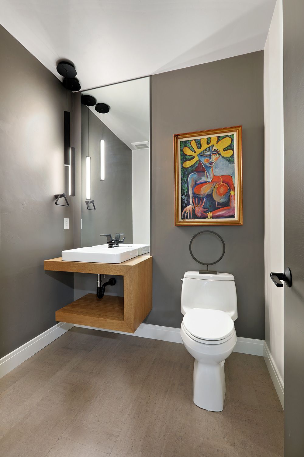 A bathroom with a toilet , sink , mirror and painting on the wall.