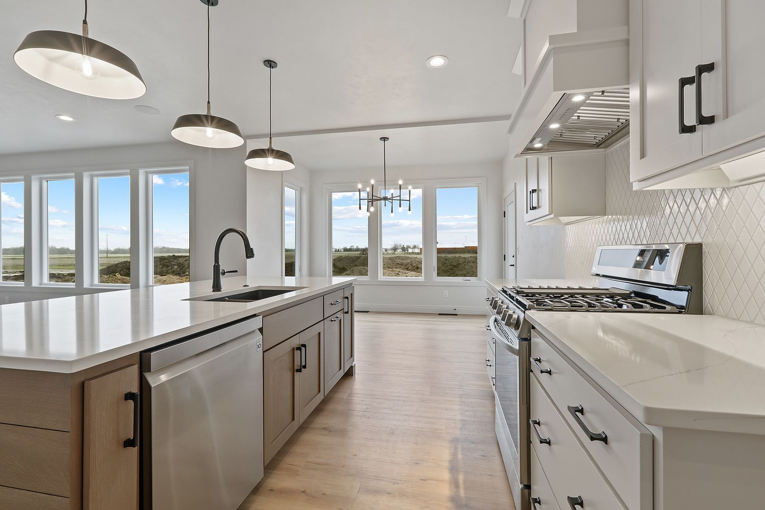 Bright, modern kitchen with white cabinets, island, stainless steel appliances, and large windows offering a view.