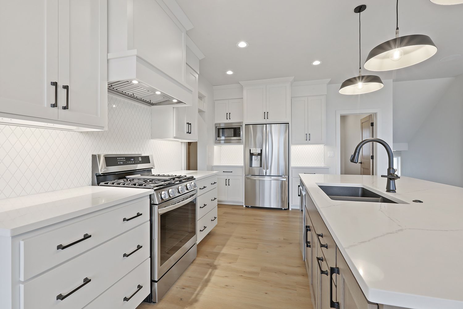 White modern kitchen with stainless steel appliances and light wood floors.