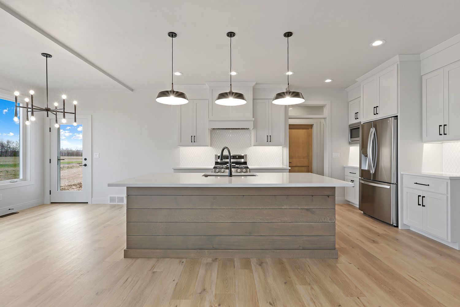 Modern kitchen with white cabinets, large island, pendant lights, stainless steel appliances, and hardwood floors.