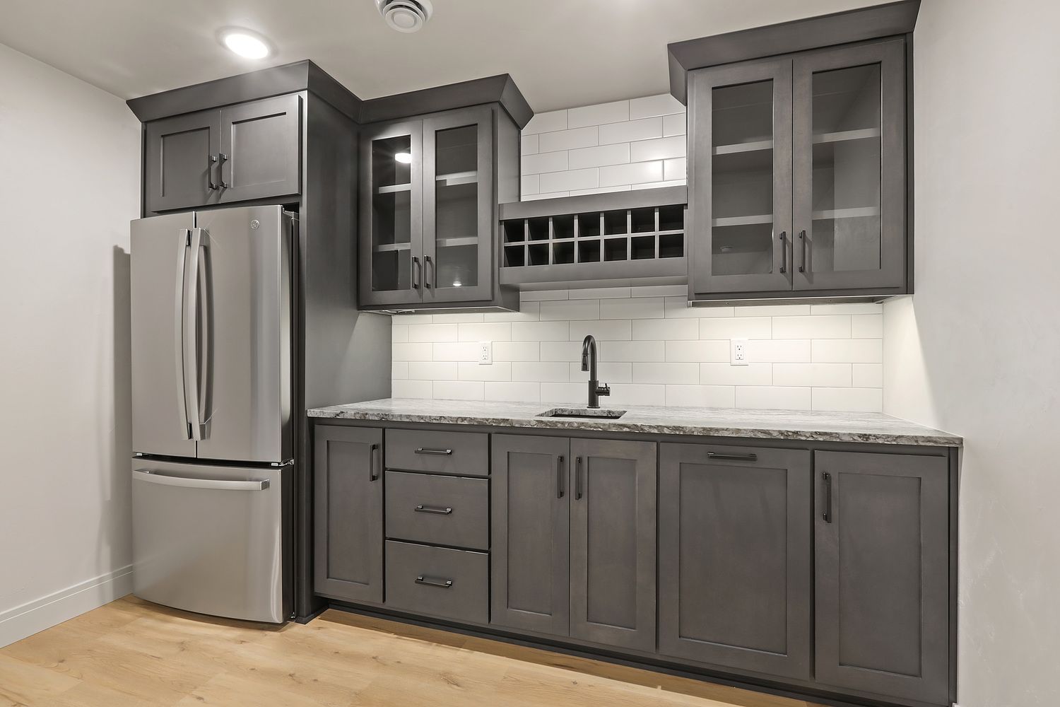 Gray cabinets with a refrigerator, sink, and wine rack built into a wall.